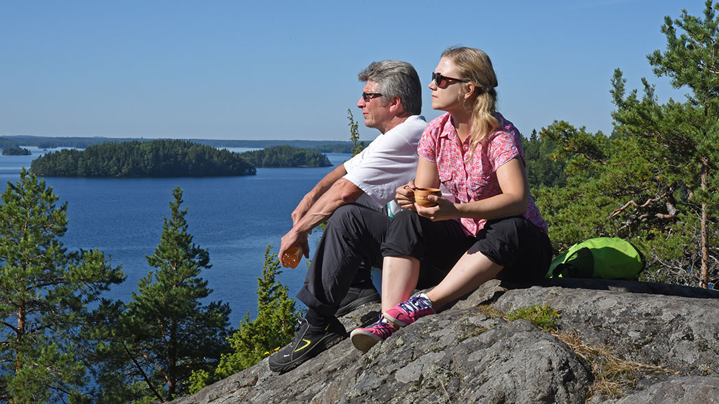 Två vandrare sitter på en klippa. Sjölandskap i bakgrunden.