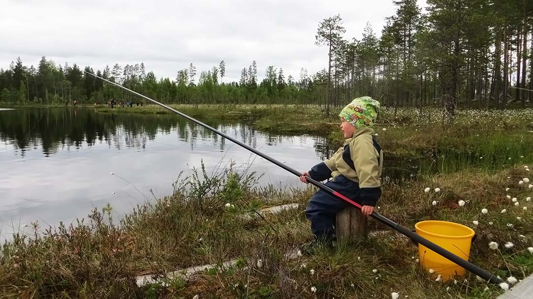 Ett barn sitter med ett fiskespö vid sjöns strand.