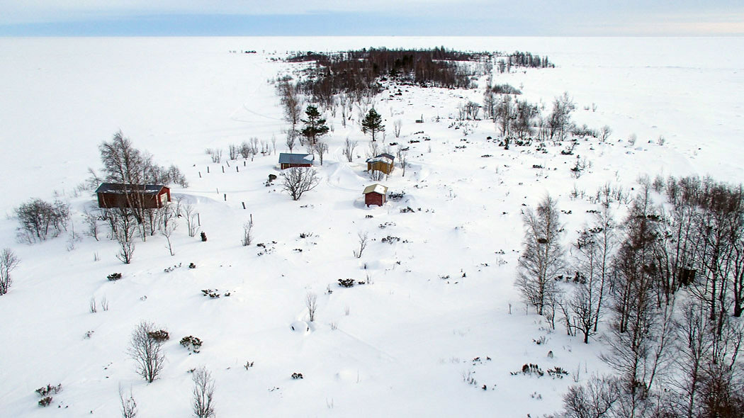 Ett snöigt havslandskap och en ö, på ön finns byggnader. Fotografiet är taget ovanfrån ett torn på ön.