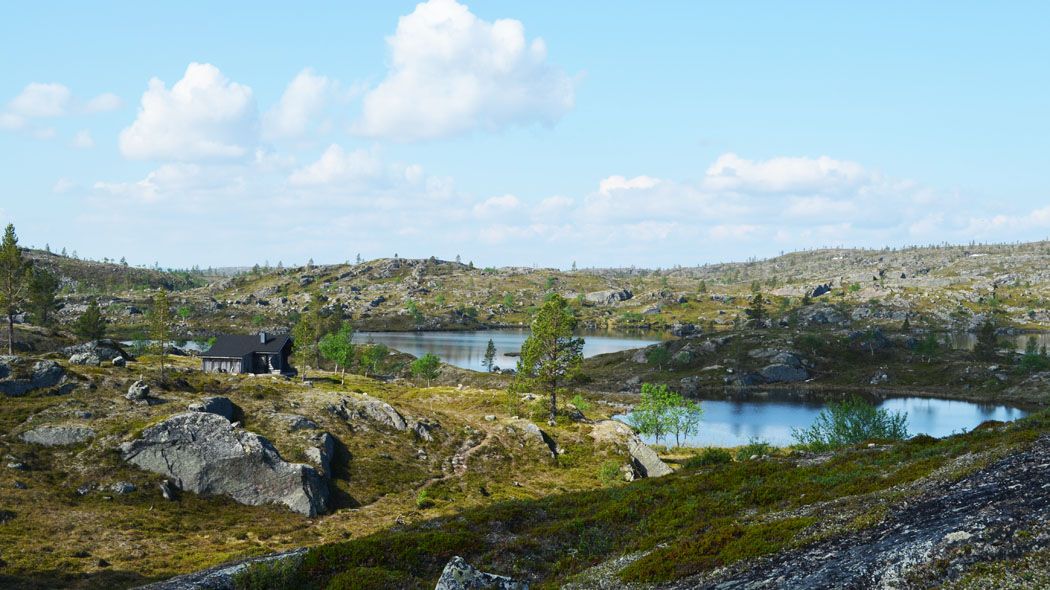 Ett stenigt fjällandskap där några små sjöar kan ses. Det finns en ensam liten stuga nära sjöarna.