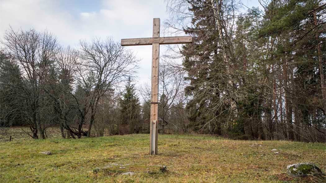 Ett stort träkors på ängen. Skog i bakgrunden.