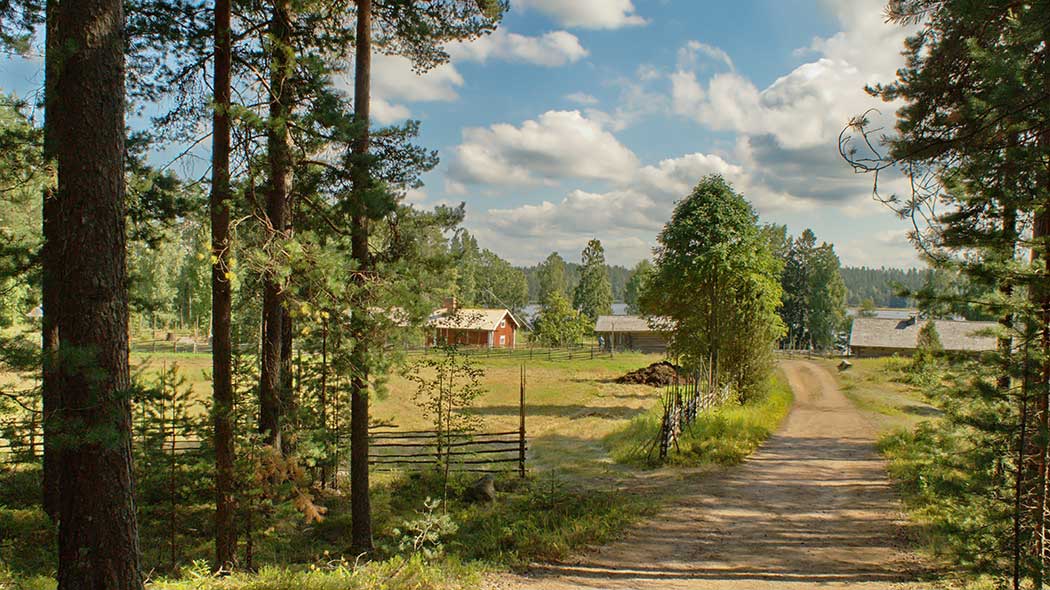 En sandväg leder från tallskogen förbi en betesmark omgiven av ett slanstaket till en gammal gårdstun. På gården finns en röd huvudbyggnad och grånande utebyggnader. Några moln kan ses på den blå himlen.