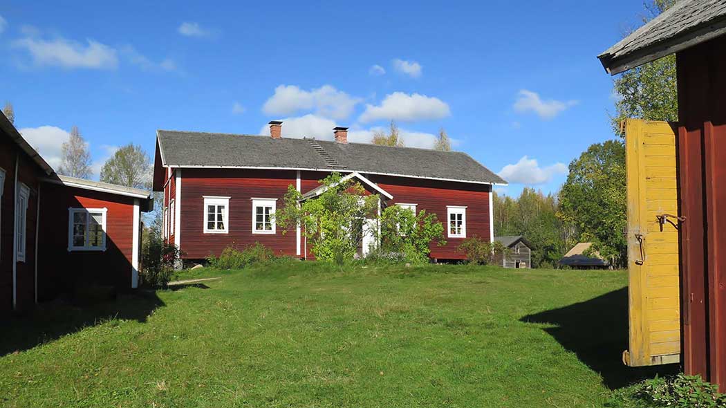 Sommarlandskap av en traditionell lantgård. Det finns byggnader i bakgrunden.