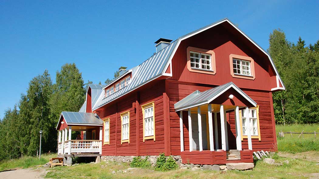 En gammal träbyggnad och dess gård en solig sommardag.