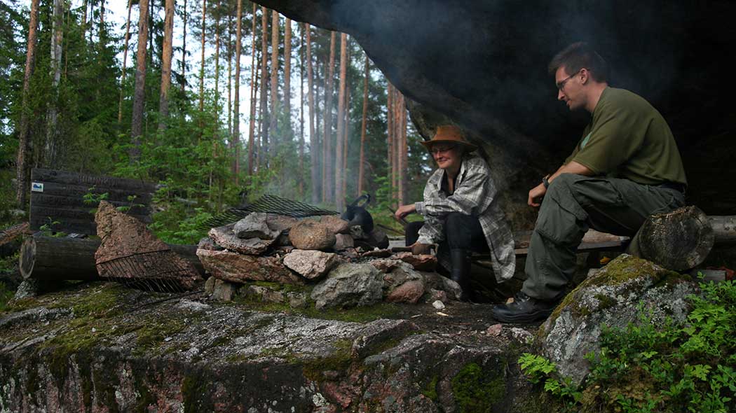 Två vandrare vid en eldplats under ett överhäng i ett flyttblock.