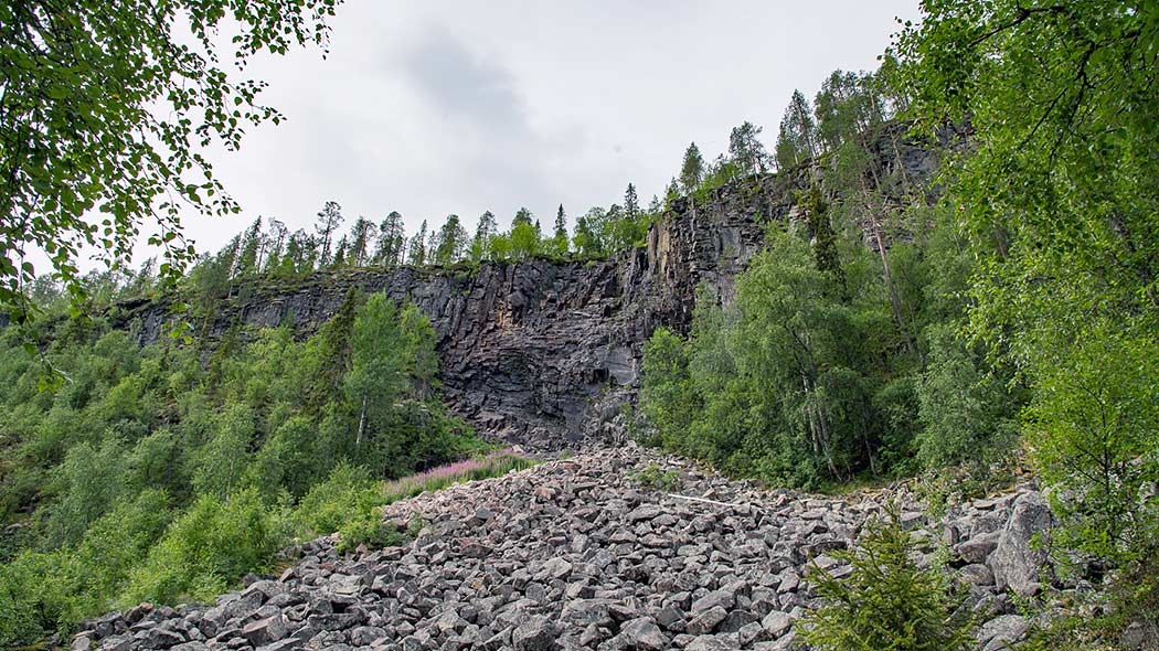 En brant klippa med en hög sten i bakgrunden.