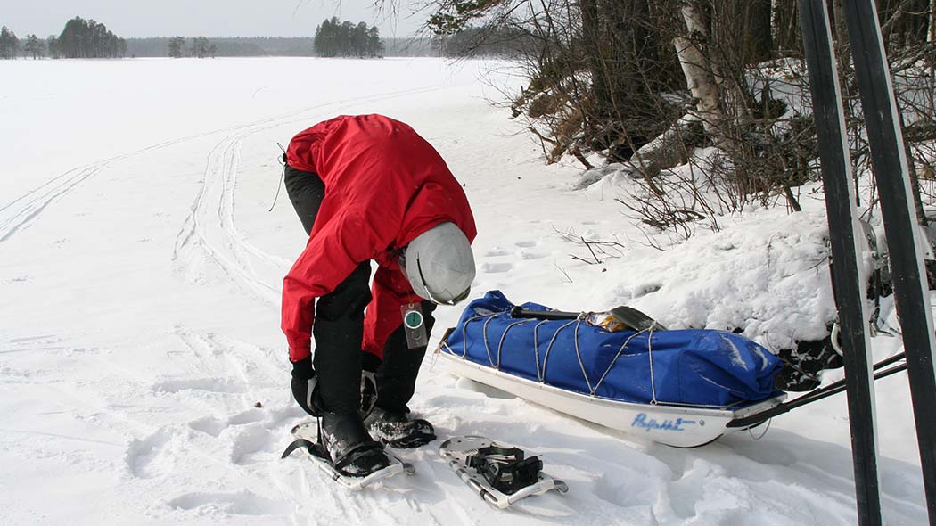 En vandrare som tar på sig snöskor på sjöstranden.