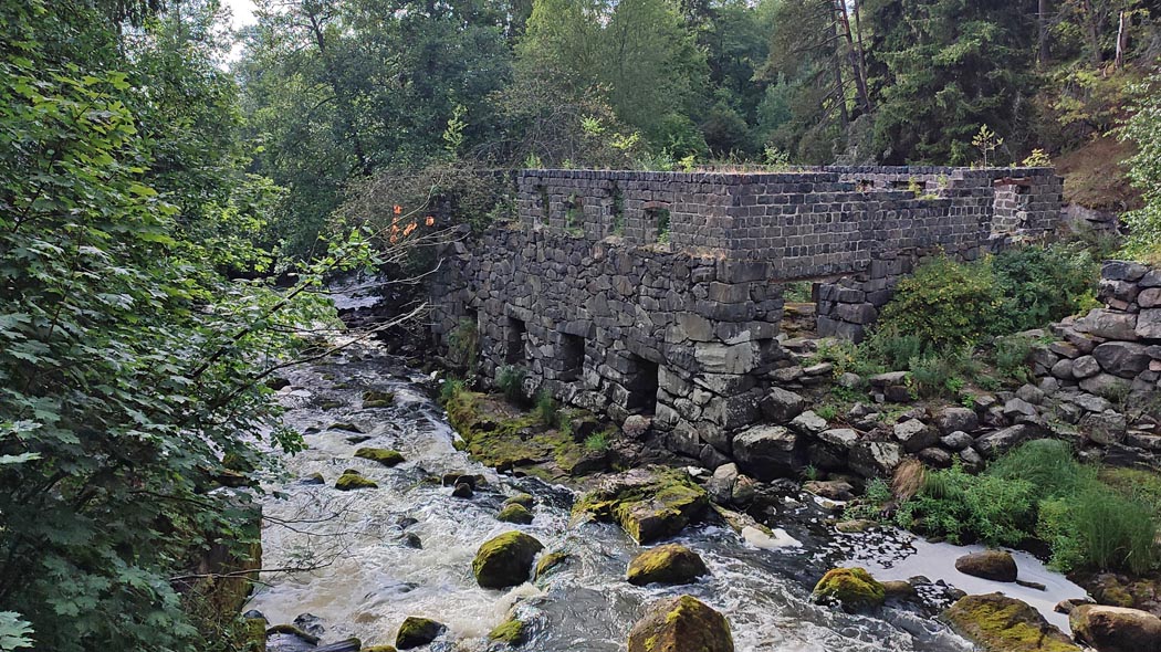 Den steniga ruinen invid den strömmande forsen. Längsmed forsens grön vegetation.