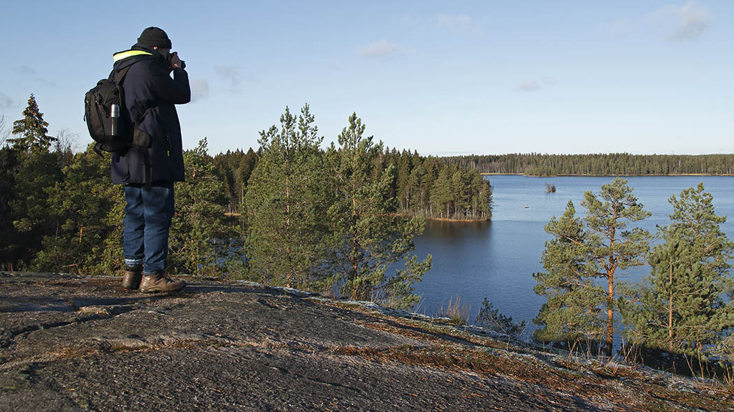 En vandrare står på ett berg och blickar ut mot sjön som är omgiven av skogar.